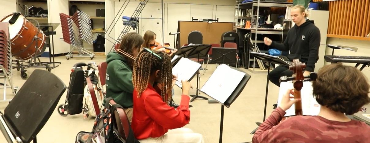 Mr. Altman directs students playing string instruments in the band room